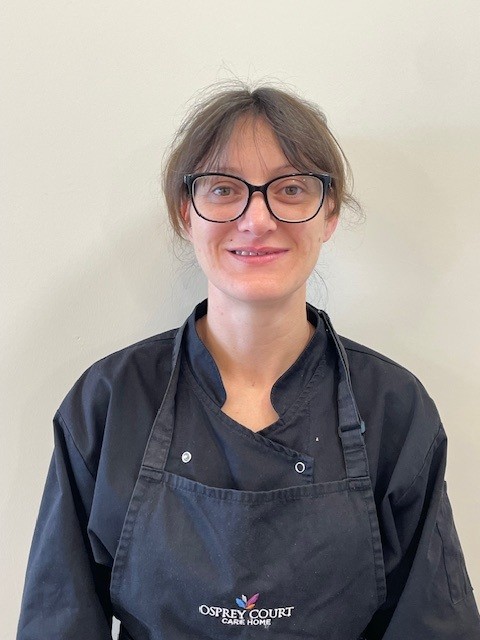 lady wearing black shirt and apron with glasses smiling at camera