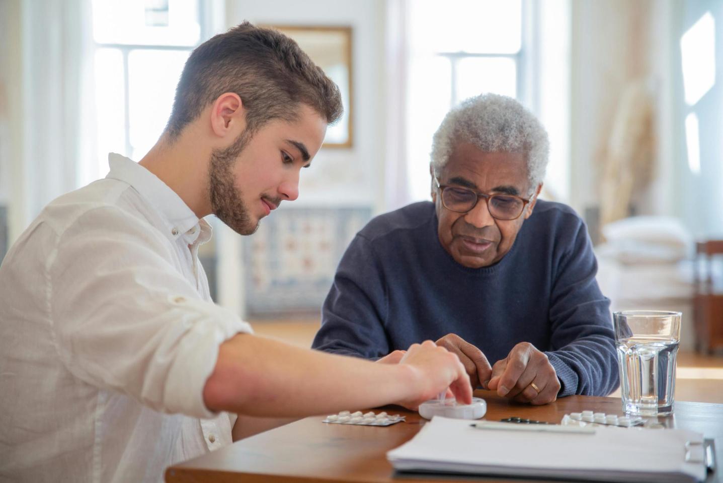 older man getting help. with taking medication by a younger man